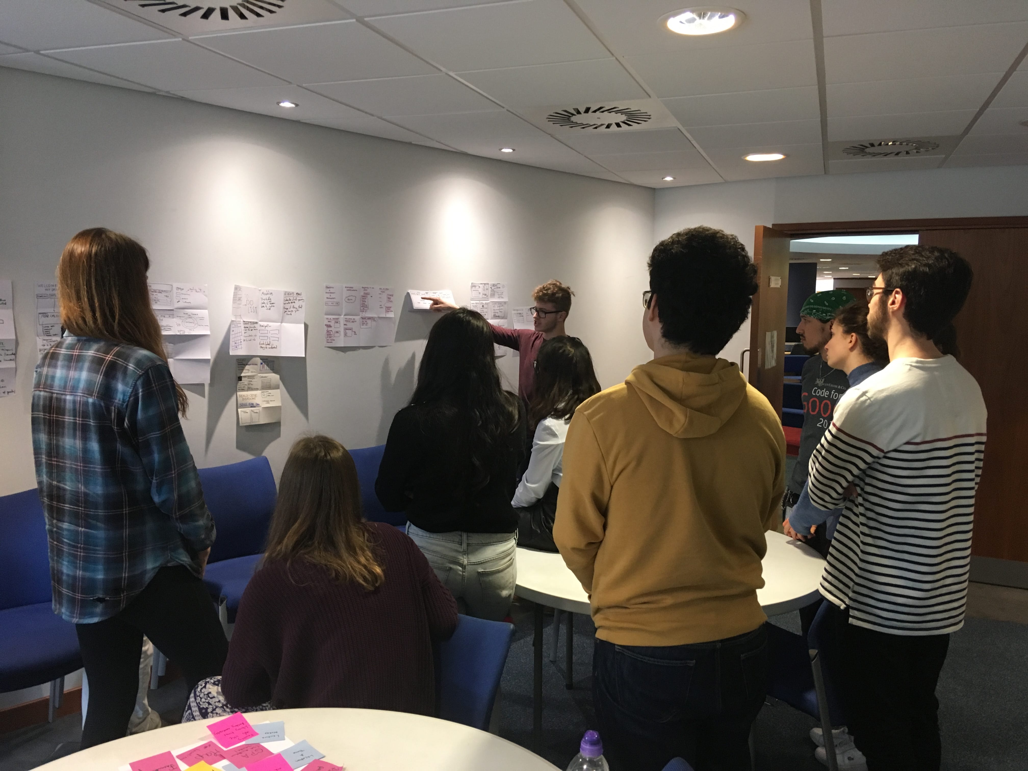 Students standing looking at design sprint ideas stuck to the wall.