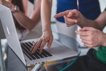 Three people's hands point to a laptop computer